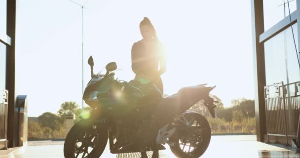 Piękny smukły sexy młoda brunetka w czarne ubrania polerowanie sportowy luksusowy motocykl na samoobsługowej myjni samochodowej o zachodzie słońca, zwolniony ruch — Wideo stockowe