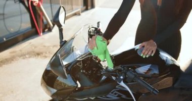 Siyahlı, narin bir kadın lüks motosikletini mikrofiberle temizliyor. Araba yıkamada, ağır çekimde.