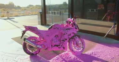 Günbatımında araba yıkama istasyonunda pembe köpükle kaplı pahalı modern motosiklet resmi.