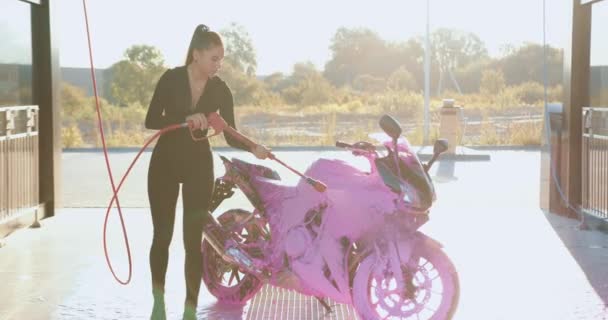 Nádherně pozitivní mladý štíhlý ženský motocyklista v černém oblečení praní luxusní motocykl s pěnivým roztokem pomocí vysokotlakého proudu na samoobslužné mytí aut — Stock video
