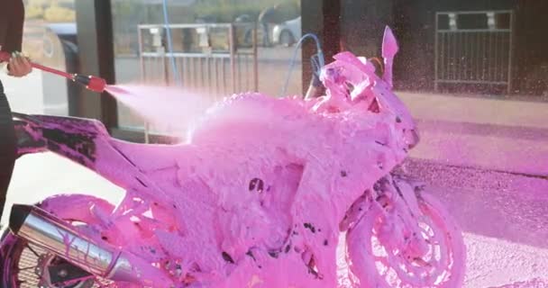 Okänd smal snygg ung kvinna täcker lyxig motorcykel med rosa skum med hjälp av högtrycksström under tvätt på utomhus biltvätt — Stockvideo