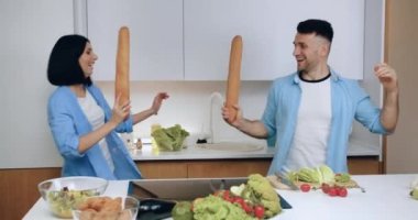 Sevimli, güler yüzlü evli çift aile yemeği hazırlıkları sırasında iyi tasarlanmış mutfakta kılıçlar gibi baget ekmeğiyle kavga ediyorlar.