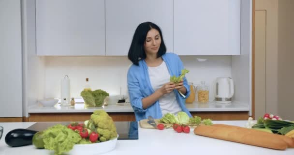 在为家庭晚餐准备新鲜蔬菜沙拉的过程中，在厨房桌子边跳舞的黑头发女人笑得很开心 — 图库视频影像