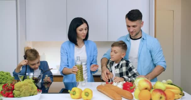 Attraktiv tilfreds positive to brødre, der hjælper deres forældre med at forberede grøntsagssalat til familiemiddag i smukt køkken, tæt på. – Stock-video