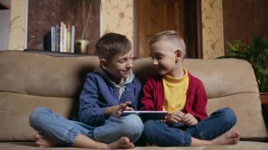 Portrait of handsome smiling excited two brothers which sitting on soft couch at home and celebrating victory in video games on tablet device and raised their hands,slow motion