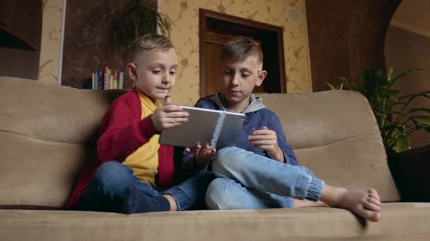 Likable satisfied modern smart boys sitting on soft couch at home and watching apps on tablet computer or playing online games ,front view,accelerated motion — Stockvideo