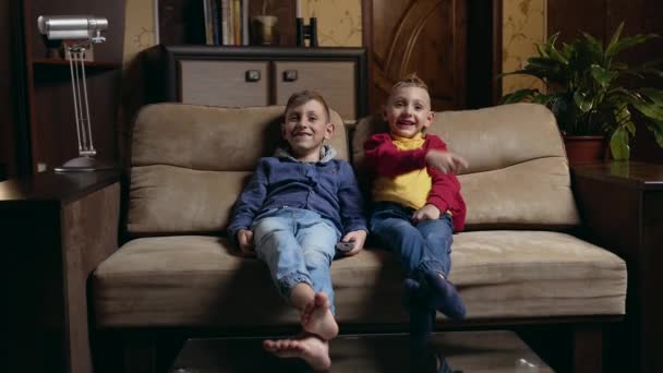 Kellemes mosolygós vidám iskolás fiúk szórakozás együtt tévénézés közben otthon, és egyikük csatornát vált a remore vezérlés — Stock videók