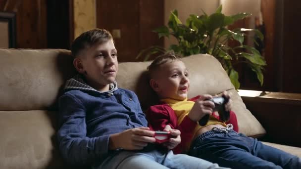 Handsome happy satisfied active schoolboys sitting on the soft couch at home and playing video games with joysticks,celebrating victory,accelerated motion — Stok video