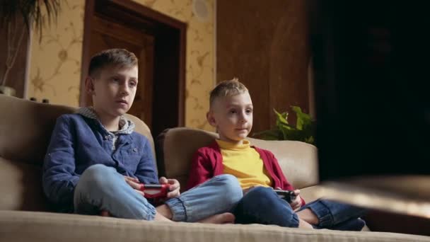Likable active positive two friends or brothers sitting on soft couch and attantivly playing video games with joysticks,spending joint leisure at home — Stock Video