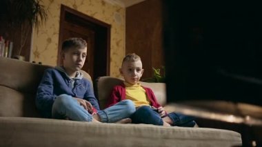 İyi görünümlü, konsantre olmuş, 10-12 yaşlarında, oturma odasındaki kanepede oturan ve oyun kağıtları kullanarak TV 'de video oyunlarından zevk alan iki çocuğa yakın durun.