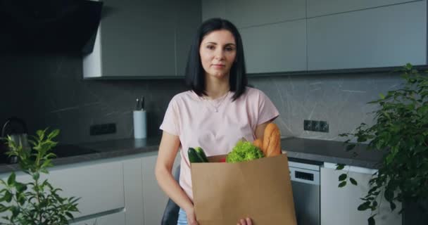 可敬的自信心情好的黑发女人看着摄像机，手里拿着她在超市或食品店里买的全套产品，放眼前方 — 图库视频影像