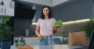 Kameranın önünde duran ve bir elinde marul yaprakları diğer elinde mango olan oldukça olumlu bir genç kadının portresi.