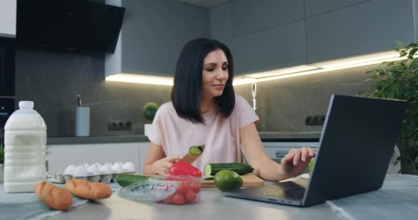 최신 요리에서 날카로운 칼을 사용하여 보드를 자르고 컴퓨터로 온라인 요리 쇼를 보며 행복하게 미소짓는 어린 브라무네들 — 비디오
