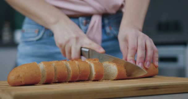 Ismeretlen nő ügyesen vágja házi kenyeret vágódeszkán a konyhaasztalon, elölnézetből — Stock videók