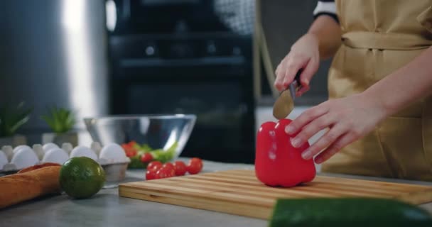 Concetto nutrizionale sano in cui donna sconosciuta che taglia mezzo peperone bulgaro con coltello sul tagliere durante la preparazione di insalata di verdure in cucina — Video Stock