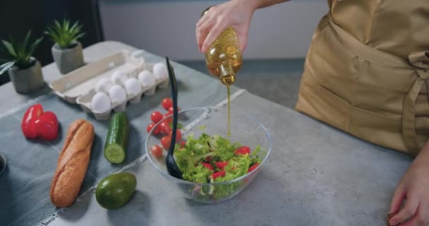 Onherkenbare huisvrouw die olijfolie toevoegt aan groentesalade in glazen kom bij de bereiding ervan in de eigentijdse keuken, zelfgemaakt bereidingsconcept — Stockvideo