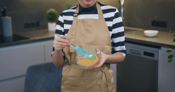 Muito positiva dona de casa de 30 anos em óculos em pé na frente da câmera enquanto mistura ovos com batedor preparando saborosa omelete para sua família — Vídeo de Stock