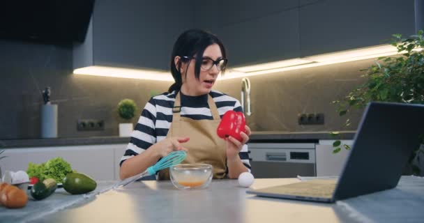 Jóképű, vidám, 30 éves barna nő, aki elmagyarázza online beszélgetőpartnerének, hogyan készítsen omlettet zöldségekkel lépésről lépésre — Stock videók
