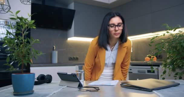 Pretty serious confident adult brunette in glasses and business clothes holding financial documents when sitting at the table in front of computer when start to work at home — Stock Video