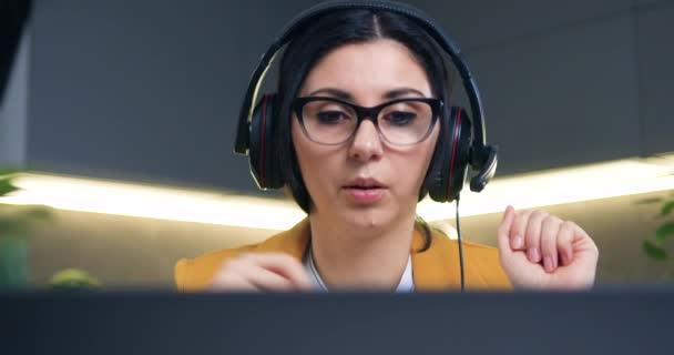 Close-up de boa aparência confiante bem sucedido 35-idade mulher de cabelos pretos em óculos no fone de ouvido que segurando videoconferência on-line no laptop de casa — Vídeo de Stock