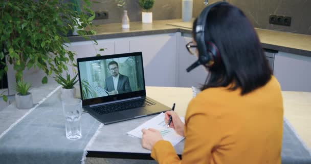 Ziemlich selbstbewusst, hart arbeitende erwachsene dunkelhaarige Frau im Headset hält Videokonferenz mit männlichen Kollegen und diskutiert mit ihm die gemeinsame Geschäftsstrategie des Projekts — Stockvideo