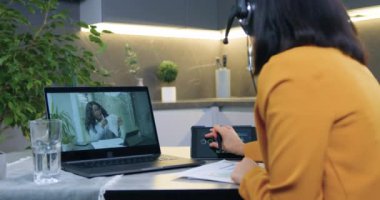 Afro-Amerikan bayan meslektaşı ile evden video konferansı düzenleyen, kulaklıklı, koyu renk saçlı, kendine güvenen bir kadın tablet cihazındaki diyagramları gözden geçiriyordu.