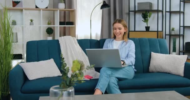 Portrait of likable cheerful modern carefree young blondie which relaxing on soft couch at home and having fun while watching comedy on laptop,leisure concept — Stock Video