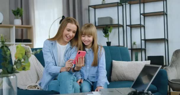 Hermosa sonrisa feliz dos diferentes edades hermanas se divierten juntos mientras pasan el ocio conjunto en casa viendo videos divertidos en el teléfono inteligente — Vídeos de Stock