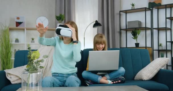 Bastante satisfecho sonriente niña de 10 años utiliza la computadora cerca de su hermana mayor interesado que gesticulando en la pantalla virtual en gafas de realidad aumentada — Vídeos de Stock