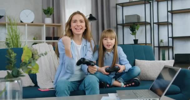 Familie vrijetijdsconcept waar goed uitziende gelukkig lachende vriendelijke twee verschillende leeftijden zussen samen plezier hebben tijdens het spelen van video game thuis met behulp van gamepads — Stockvideo