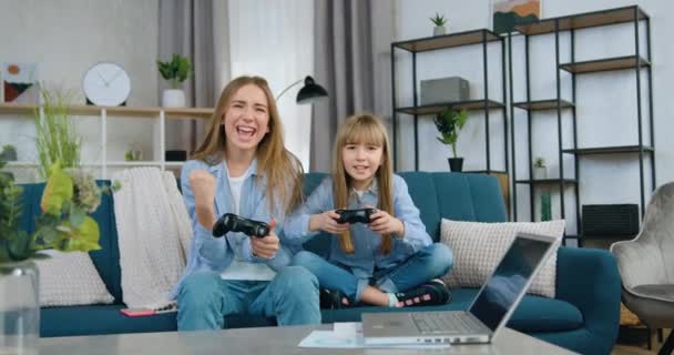 Tatmin olmuş iki kız-büyük ve küçük kız kardeşe yakın çekim. Evdeki rahat kanepede oturup video oyunlarının tadını çıkarıyorlar. — Stok video