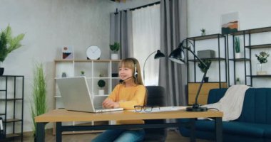 İyi görünümlü, kendine güvenen, kulaklıklı, bilgisayarının başında oturan ve uzaktan eğitim konsepti olan evden video toplantısı sırasında öğretmenle konuşan genç kız.