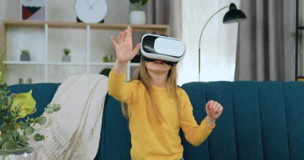 Trevlig förvånad modern 10-årig flicka med långt ljust hår i augmented reality headset gester på imaginär skärm samtidigt tillbringa fritid hemma — Stockvideo