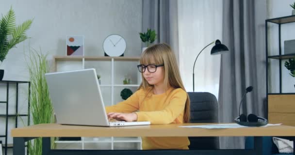 Kinderen afstandsonderwijs concept waar aantrekkelijke geconcentreerde basisschool meisje in glazen zittend achter de computer en studeren online of doen hometask thuis — Stockvideo