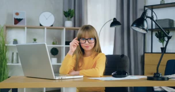 Jóképű, boldog, vidám, elegáns, 10 éves lány, hosszú szőke hajjal, pózol a kamera előtt, miközben a számítógép előtt ül a leckéi tanulmányozása közben. — Stock videók