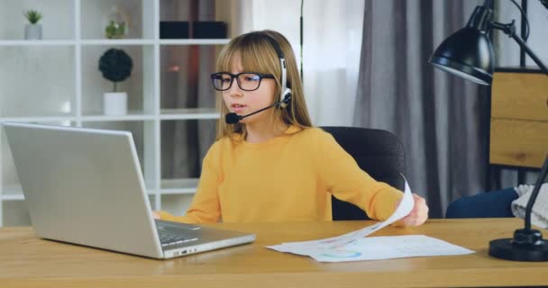 彼女の先生とオンラインビデオ会議中にグラフで彼女の宿題を示すヘッドセットで素敵な自信を持ってスマート10歳の女の子が遠隔学校教育の概念 — ストック動画