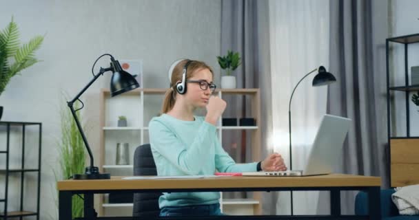 Красивая уверенная в себе молодая женщина фрилансер в очках, сидя перед компьютером дома и проведение видео-встречи с новичками, замедленная съемка — стоковое видео