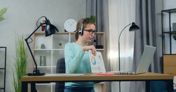 Vrij positief vertrouwen 20-jarige vrouwelijke student in hoofdtelefoon presenteren haar rapport met infographics aan universitair docent tijdens online seminar, remote education concept — Stockvideo