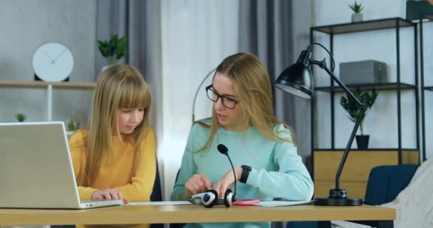 Portrait of pretty confident eldest sister in glasses which explaining how to do homework her younger sister when sitting together at workplace at home — Stock Video