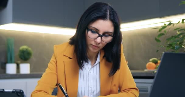 Portrait of good-looking concentrated successful adult brunette in glasses and stylish jacket which sitting at home office and working with business papers,remote work concept — Stock Video