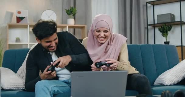 Dobře vypadající spokojený zábavný multihnic pár baví spolu při hraní videoher, žena v hidžábu slaví vítězství, vousatý chlap je naštvaný, protože ztratil — Stock video