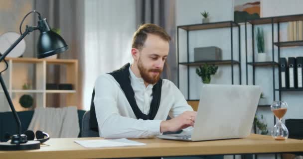 魅力的な自信を持ってスタイリッシュな結婚式のひげを生やした男が自宅でテーブルに座ってコンピュータで作業し、フロントビュー — ストック動画