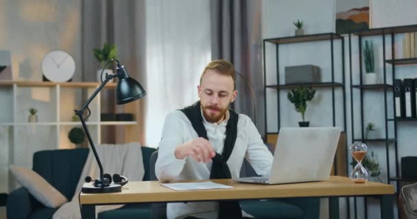Sandsynlig koncentreret erfaren ung skægget mand sidder foran bærbar computer i hjemmekontoret og indtastning af data fra rapport, fjernarbejde koncept – Stock-video