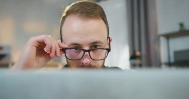 Çekici özgüvenin ön görüntüsü, iş yerinde dizüstü bilgisayarının önünde oturan ve bilgi okuyan 30 yaşında, sakallı, gözlüklü bir adama odaklandı.