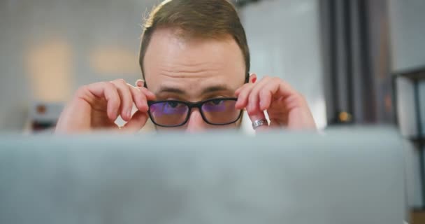 Hezký sebevědomý mladý vousatý ženatý muž si sundává brýle a zavírá notebook, když dokončí práci na něm, pracovat doma koncepce, zblízka — Stock video