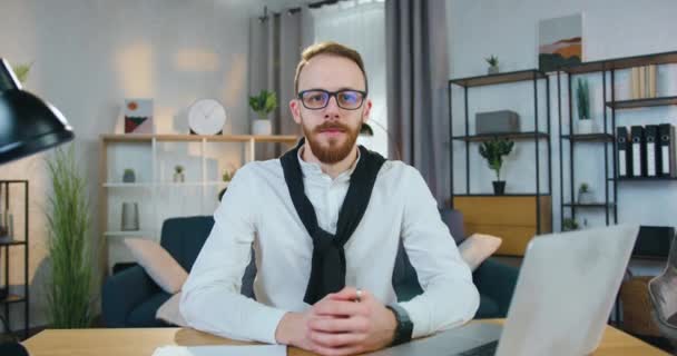 Likable positive satisfied confident young bearded man in office clothes poses on camera with thumbs up on the home office background,front view — Stock Video