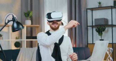 Özel 3D gözlüklü, yetenekli ve modern sakallı bir adam iş yerinde otururken sanal ekranda çalışıyor.