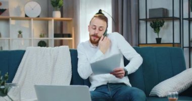 Yakışıklı, konsantre olmuş, sakallı genç bir işçi. Evdeki koltukta oturuyor ve iş arkadaşı ya da iş ortağıyla telefonda konuşurken finansal belgeleri gözden geçiriyor.
