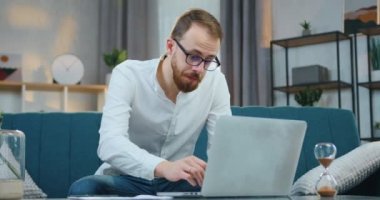 Sevimli, konsantre olmuş, 30 yaşında sakallı bir adam evdeki koltukta oturuyor ve bilgisayarda mali raporlarla karşılaştırma yapıyor.