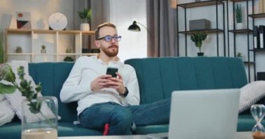 Hayalperest, mutlu, yakışıklı, sakallı, evli bir adam evdeki yumuşak koltukta oturuyor ve karısına akıllı telefondan mesaj yazıyor.